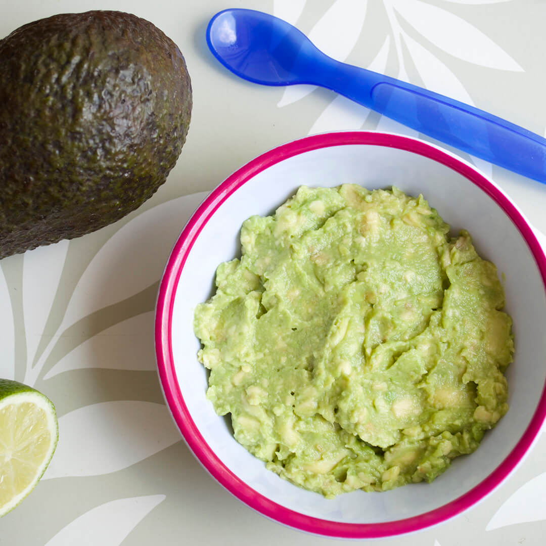 A bowl of avocado puree next to a whole avocado