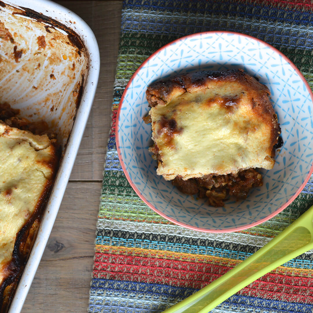 Greek moussaka in a small bowl, next to a casserole dish of moussaka