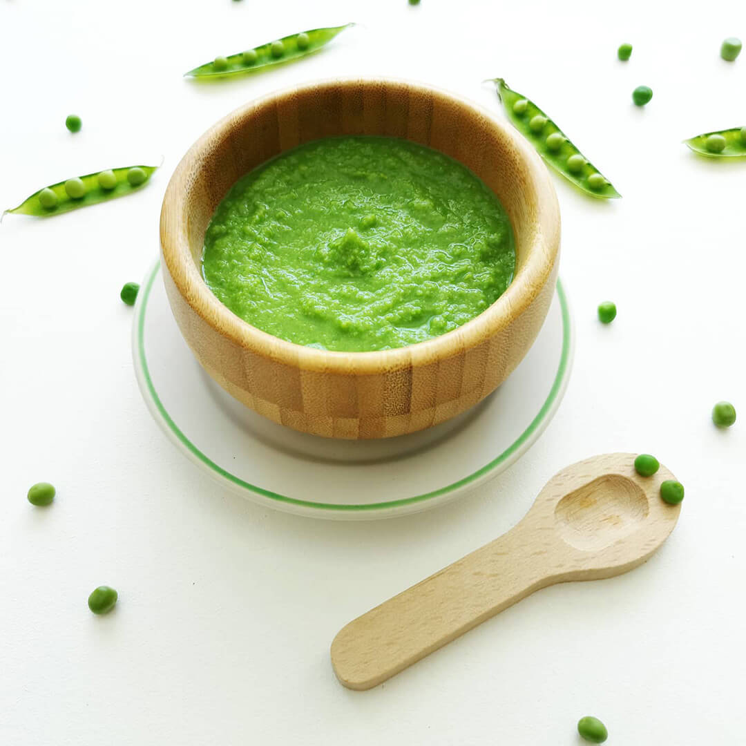 Pea puree in a small bowl with some peas around it
