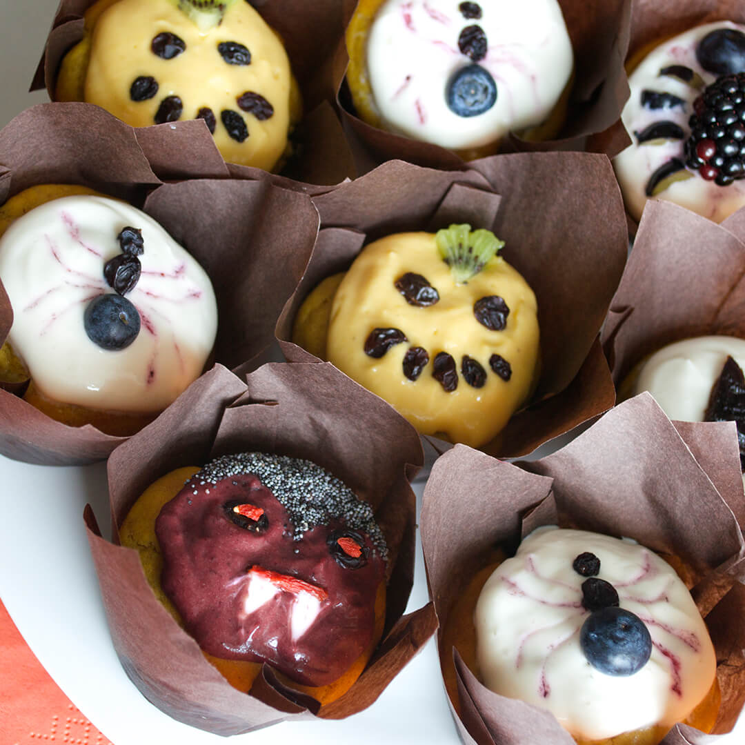 Sweet Halloween Pumpkin Muffins on a plate. Some of them are decorated like spiders, some are pumpkins and one is a vampire