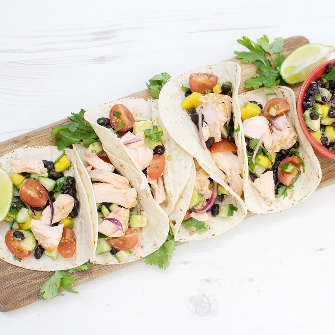 6 fish tacos on a wooden platter, served with fresh coriander, mango salsa and a wedge of lime