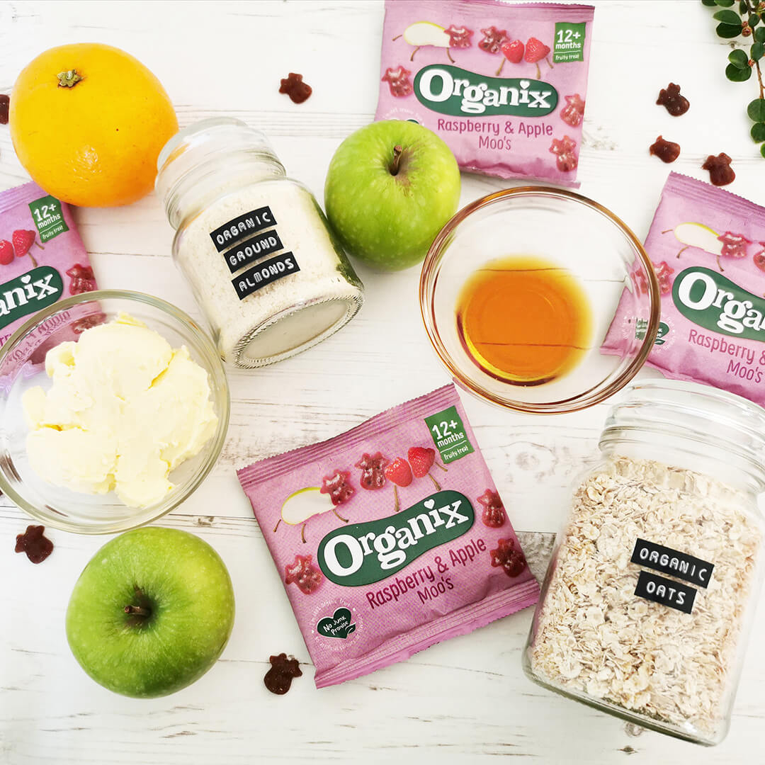 3 Organix Gummies packs next to a jar of oats, 2 green apples, a jar of ground almonds, an orange, a small bowl of butter and a small bowl of maple syrup