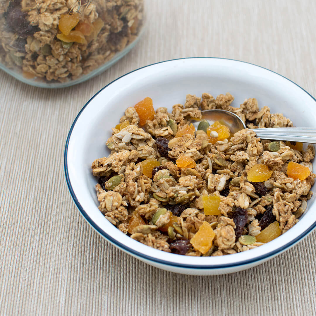 A bowl of Spiced Apricot Granola next to a glass jar of granola