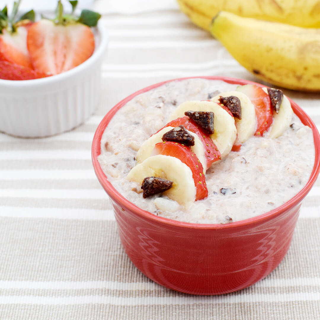 A bowl of rice pudding topped with sliced strawberries and bananas, next to a ramekin of sliced strawberries and some bananas