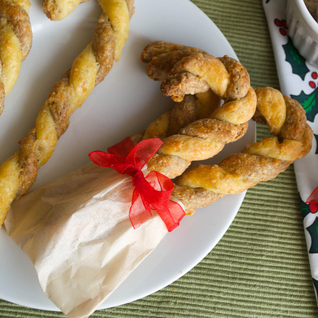 A plate of 5 Cheese Straw Christmas Canes, 3 of them are wrapped in brown paper and tied with a red ribbon