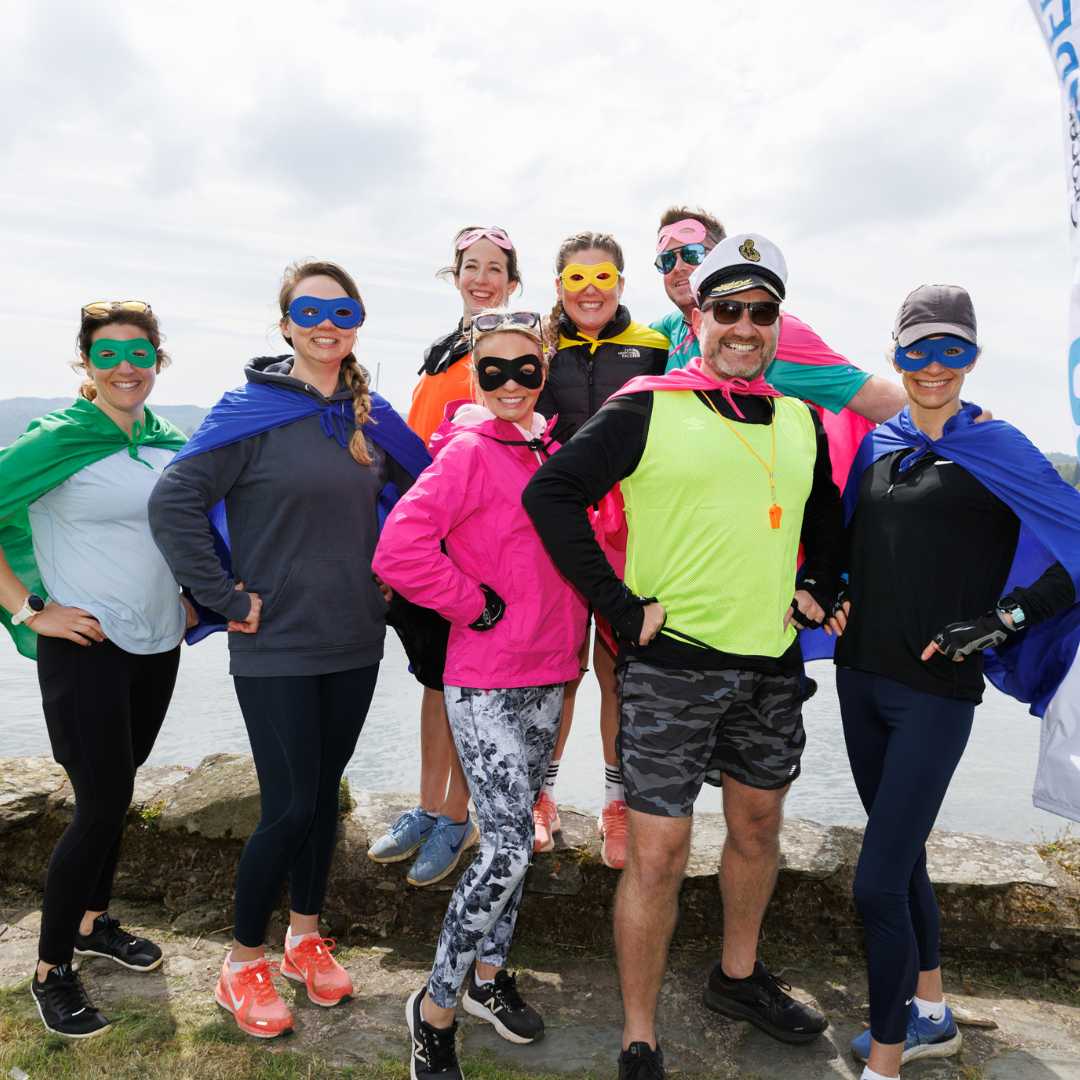 Organix employees at rowing challenge standing in a group wearing super hero capes and masks