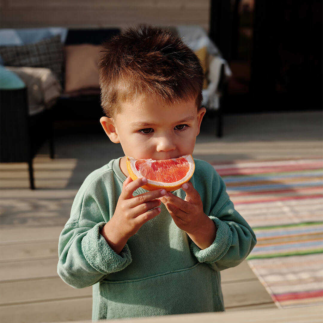 Child outdoors in the garden eating a grapefruit