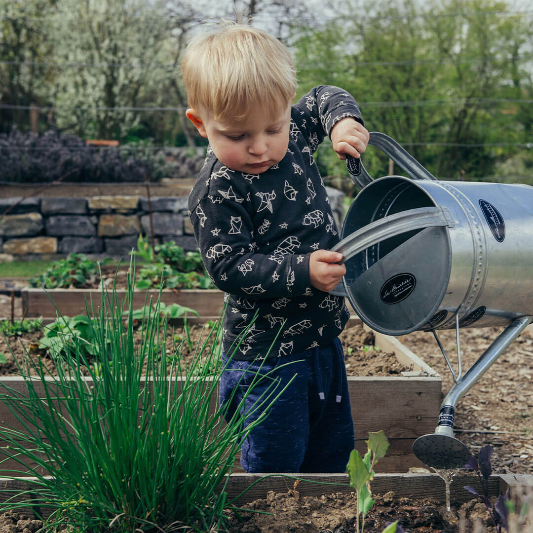 A toddler watering some plants with a watering can