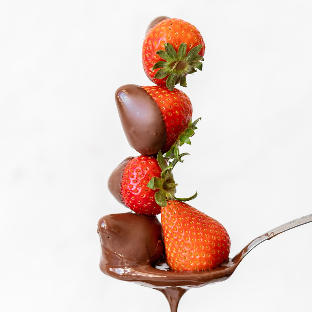 5 milk-chocolate dipped strawberries stacked and arranged on a spoon
