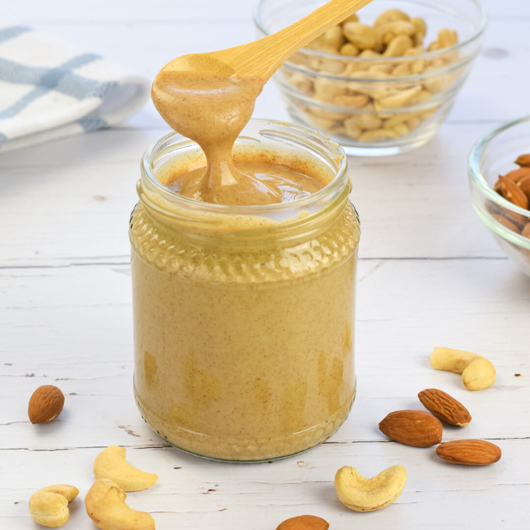A jar of almond-cashew butter next to small glass bowls of cashews and almonds