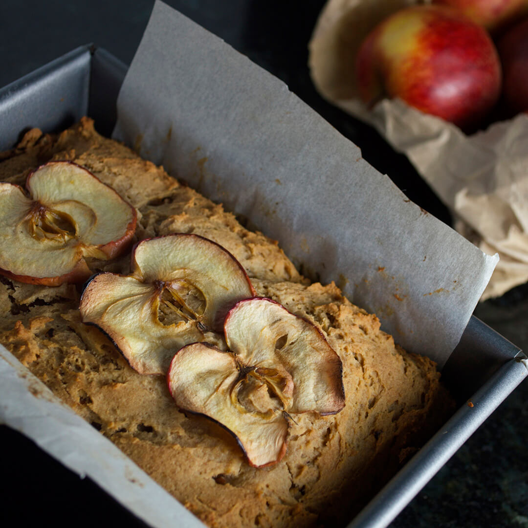Apple and ginger loaf in a baking tin next to some apples