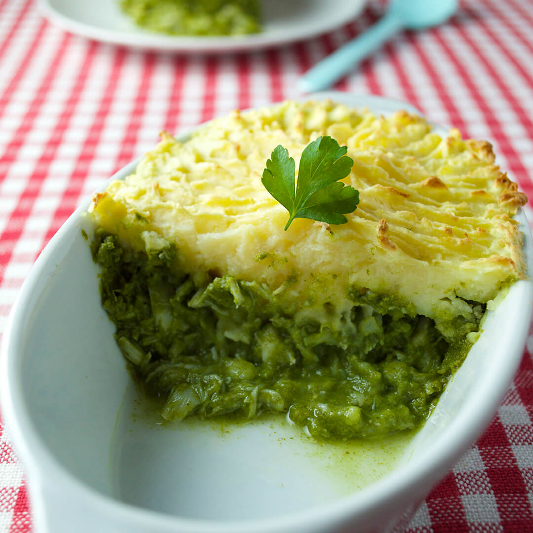 A casserole dish of fish pie with watercress sauce, next to a serving of fish pie