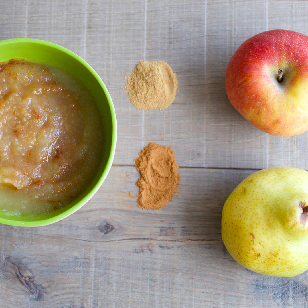 A bowl of Spiced Apple & Pear puree next to a whole apple and pear and some cinnamon