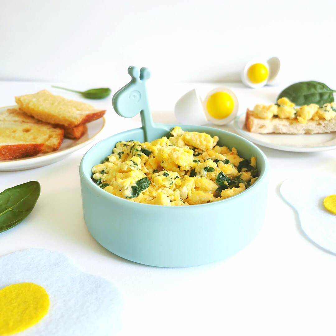 A bowl of scrambled eggs with spinach next to a plate of toast