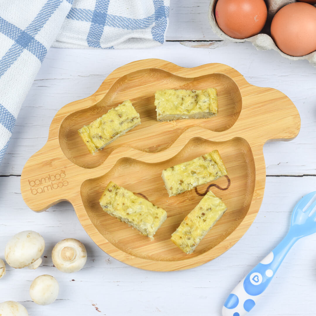 A serving of baby mushroom omelette squares next to a case of eggs and some mushrooms