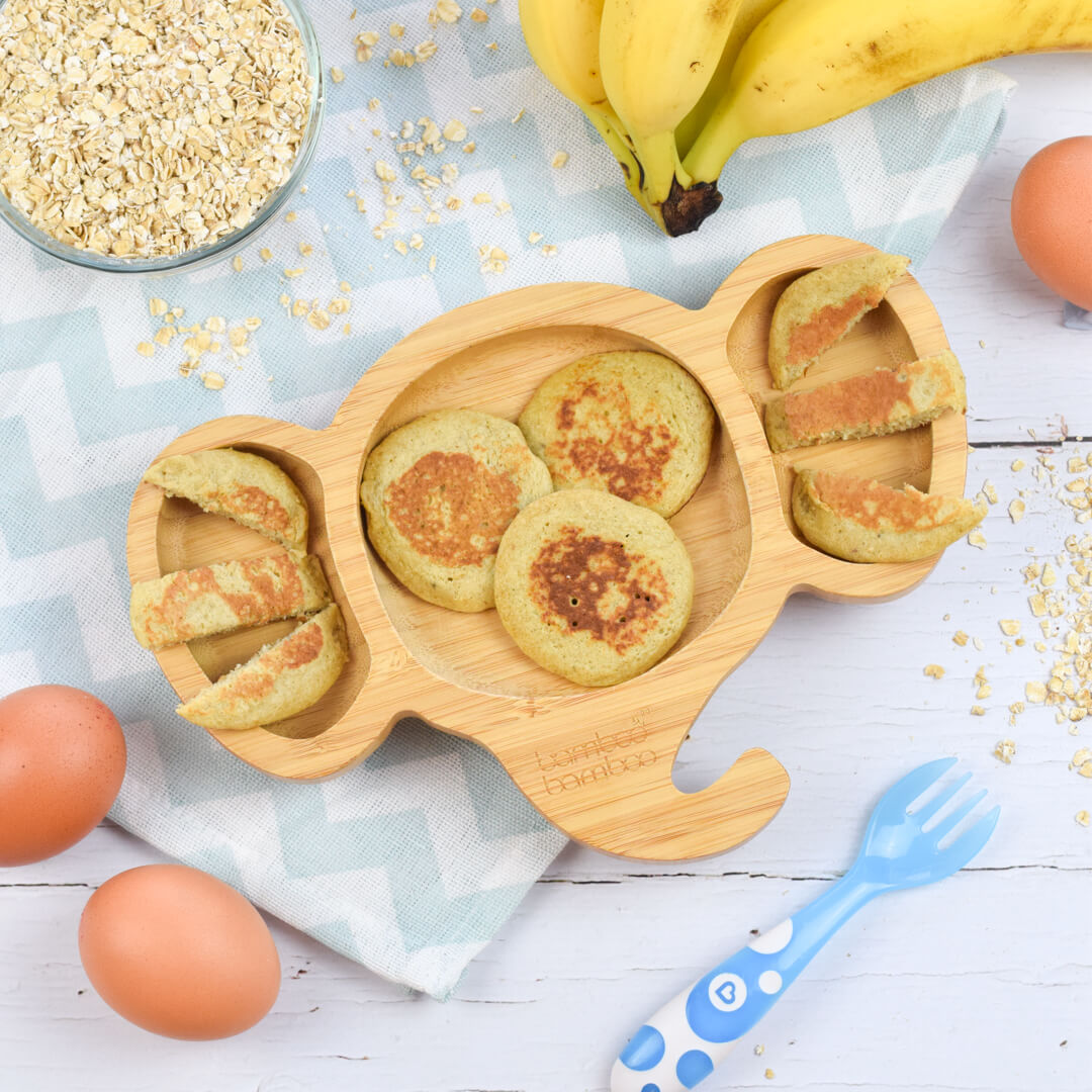 A serving of oat pancakes next to a bowl of oats, some eggs and a bunch of bananas