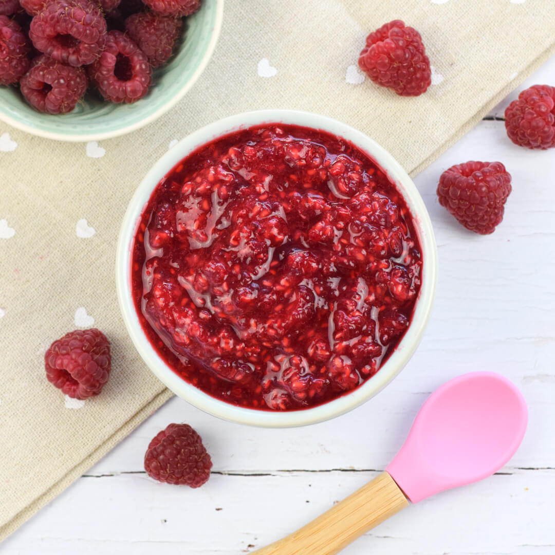 A bowl of mashed raspberries next to a bowl of whole raspberries