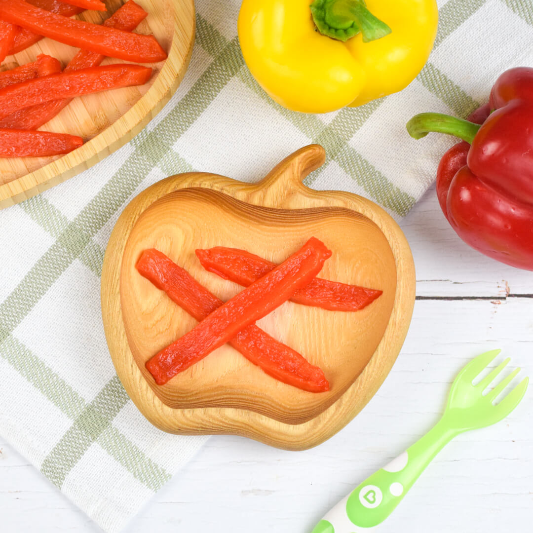 A serving of steamed red pepper next to a whole yellow and red pepper