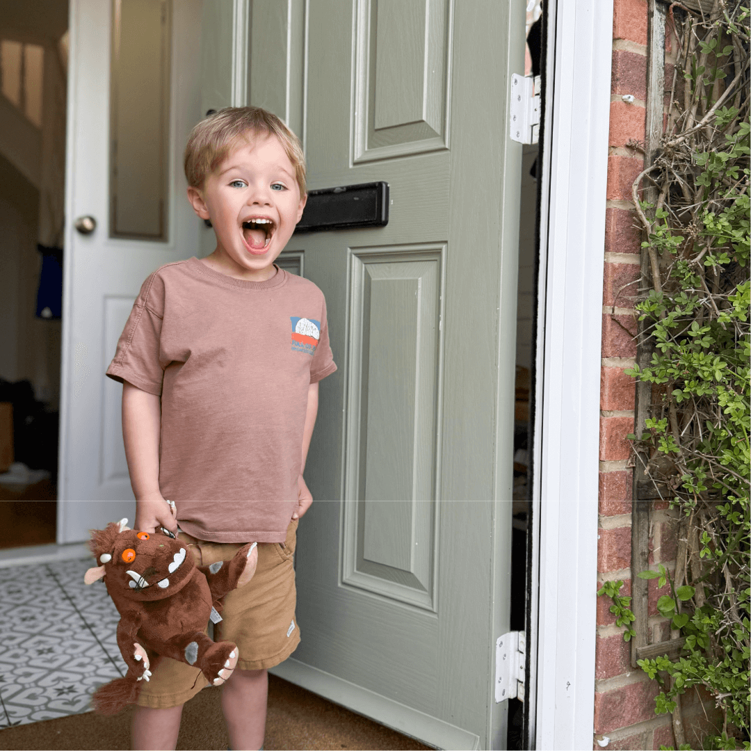 Child opening a door with a Gruffalo toy in their hand. The child has an excited expression on their face. 