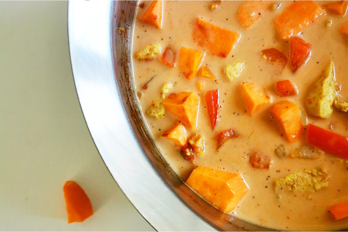 A saucepan of onions, carrots and peppers with coconut milk, sweet potato, tomato puree and curry powder