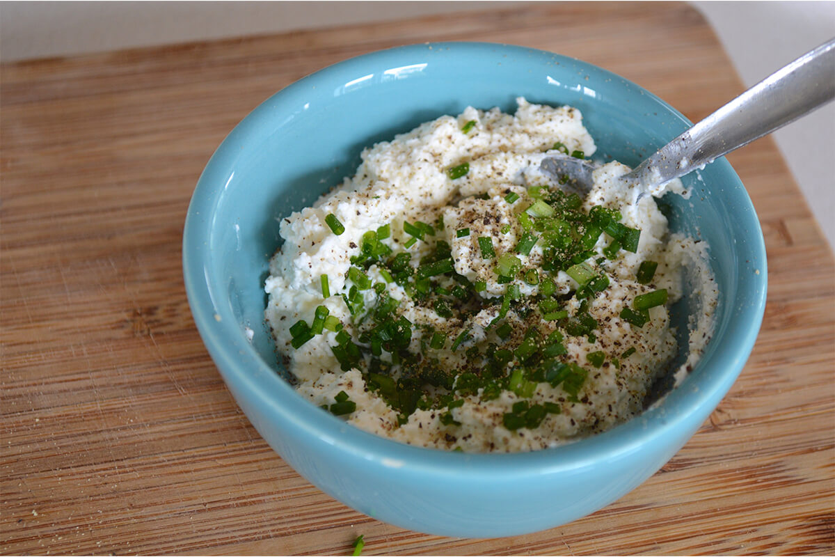 A bowl of cream cheese, chives and ground black pepper being mixed