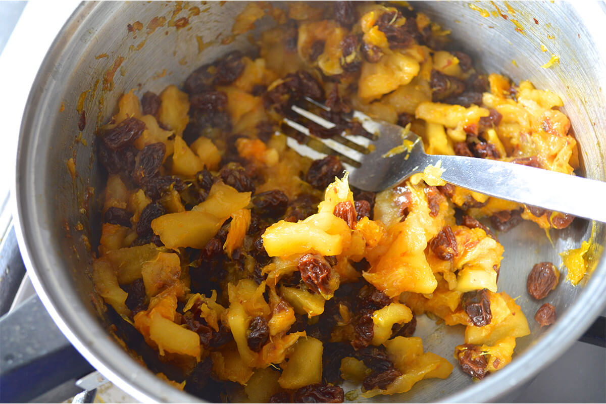 A saucepan with peeled and diced apple and oranges, raisins and honey