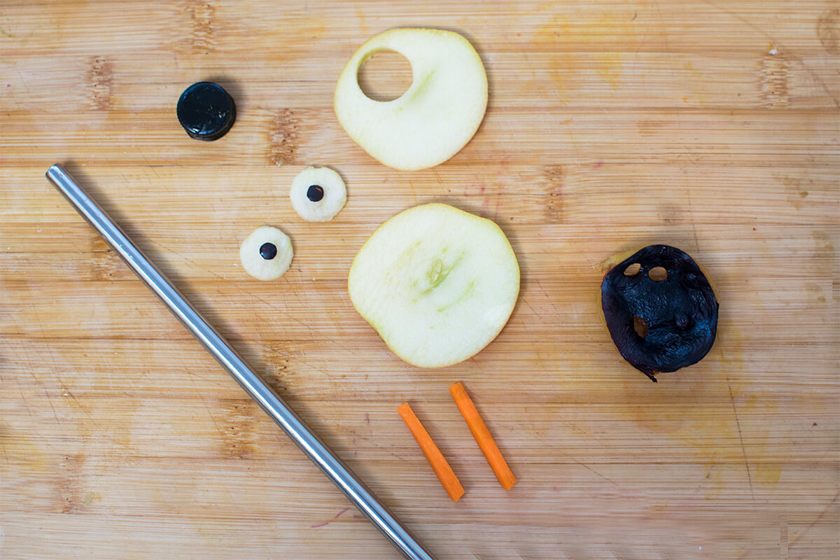 A chopping board with some apple slices, carrots and plums