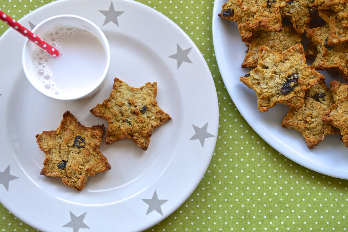 A plate of 2 honey baked stars with a cup of milk with a red straw in it, next to a plate of more honey baked stars