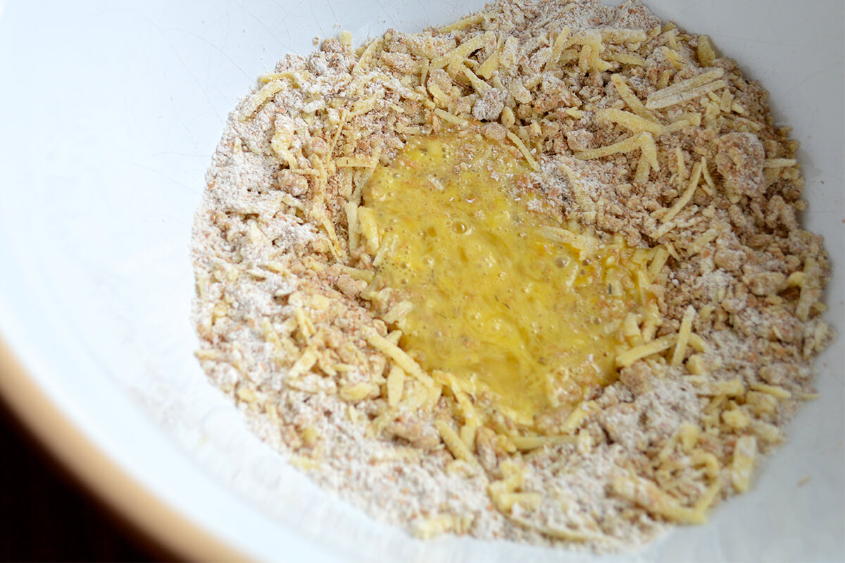 A bowl of flour with butter, cheese, thyme and egg