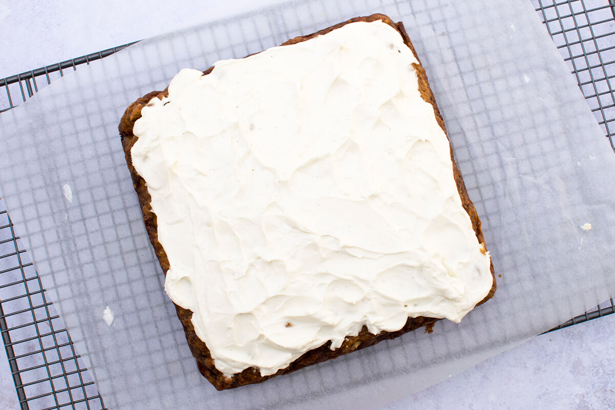 Carrot cake in a cooling rack, topped with cream cheese frosting