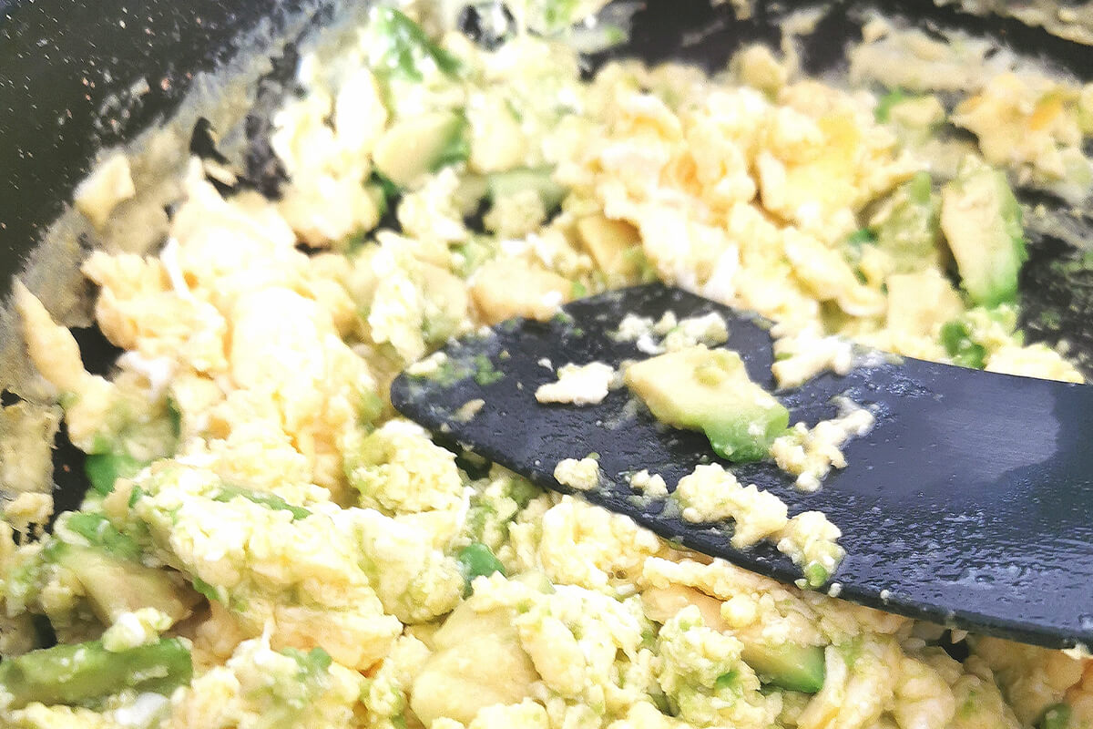 A pan of eggs being scrambled with avocado
