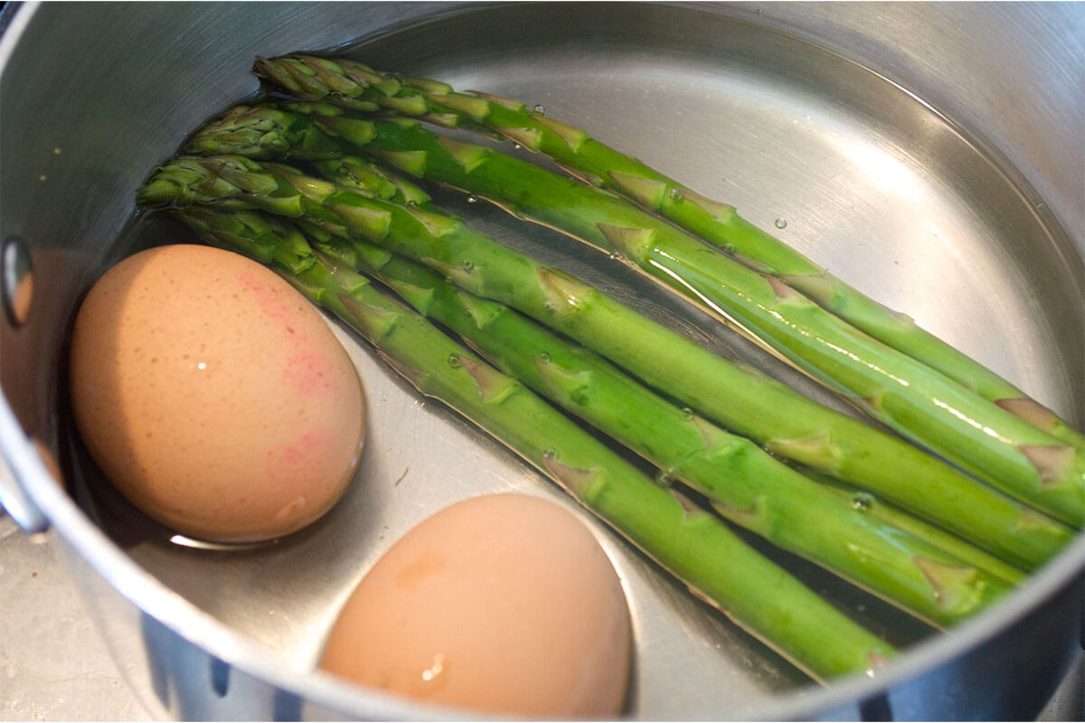 A saucepan with 2 eggs and some asparagus