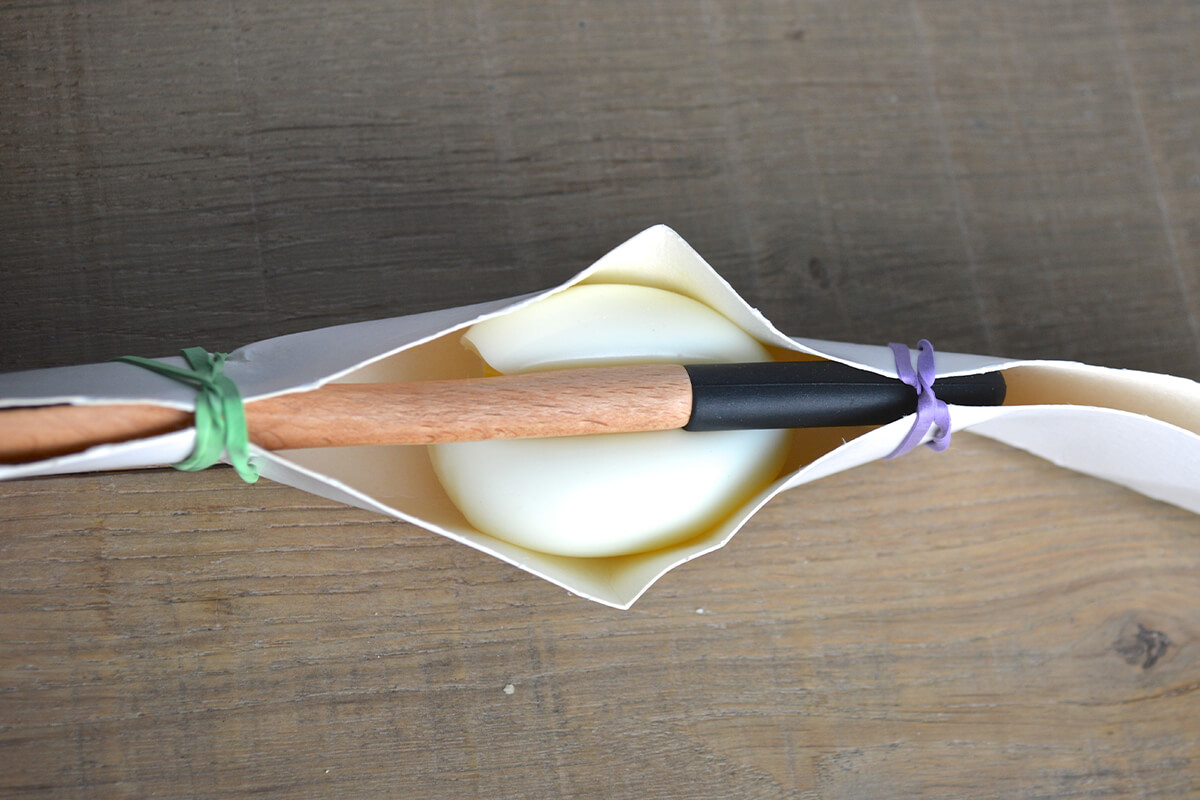 A boiled egg wrapped in strong card with a wooden skewer through the middle of it, fastened on either end with elastic bands