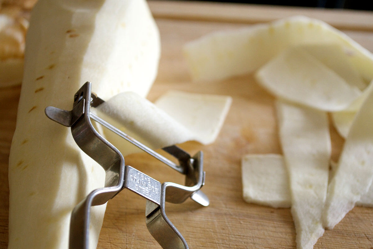A chopping board with a parsnip being peeled to make long stirps