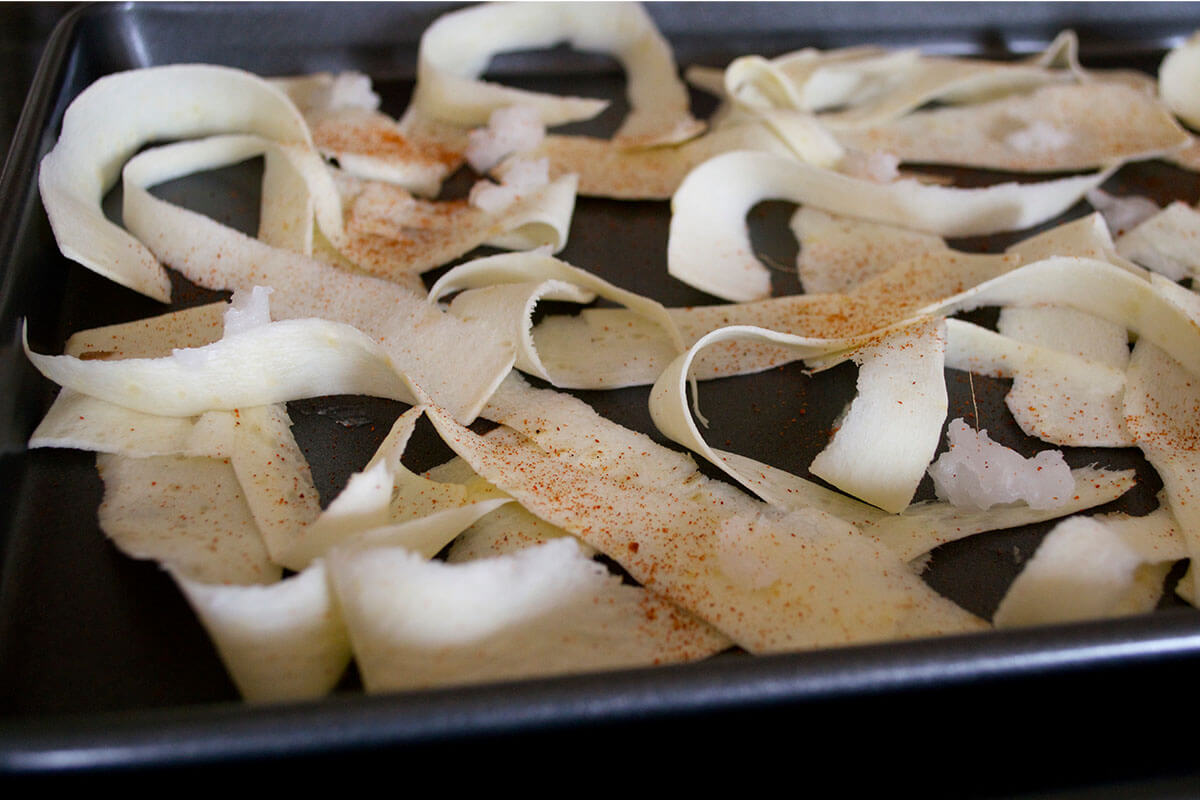 Peeled parsnip strips on a baking tray drizzled with oil and topped with paprika