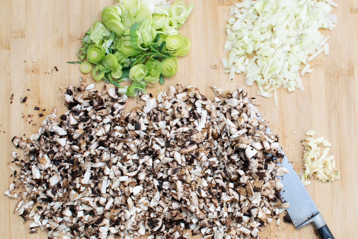 A chopping board with chopped onion, garlic, mushroom and leek