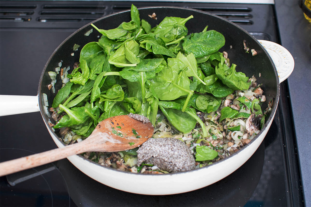 A frying pan with chopped garlic, onion, mushroom and leek with spinach leaves and chia seed "egg"