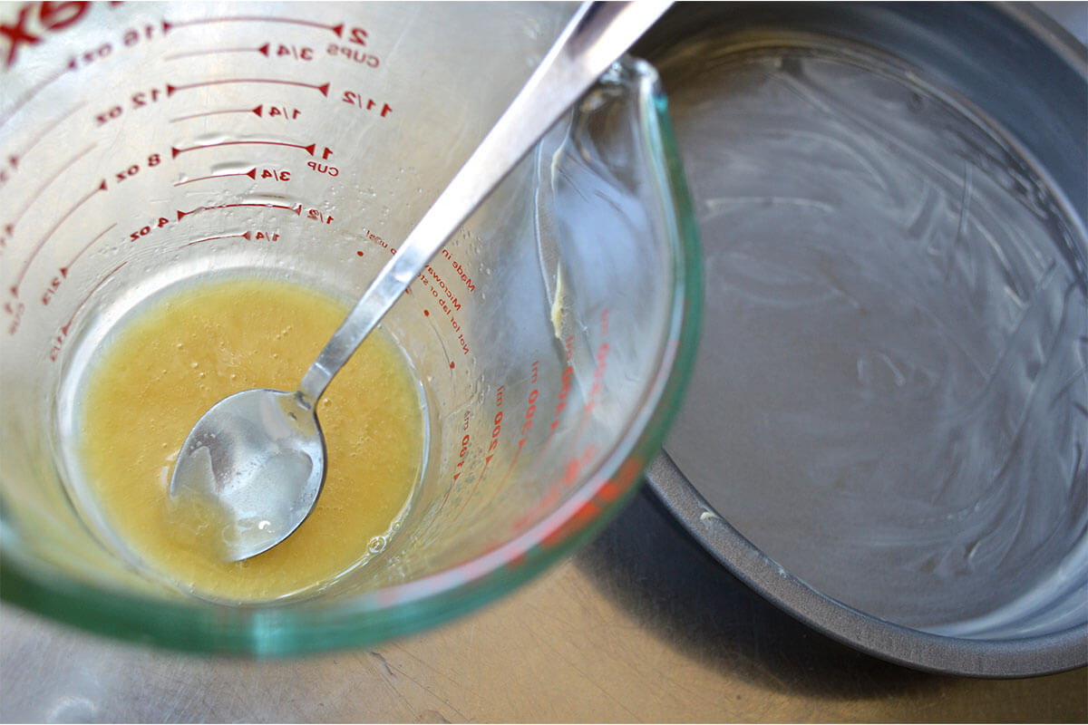 A greased cake tin next to a glass jar of honey mixed with water