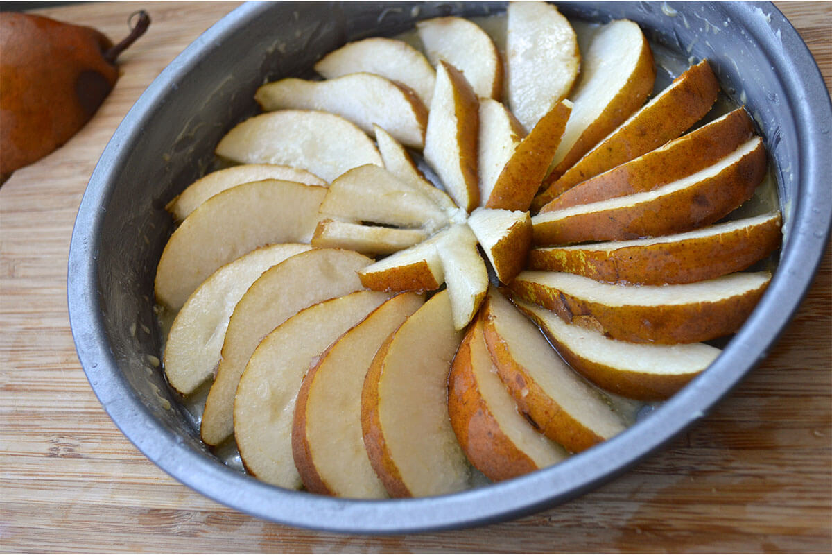 A greased cake tin with some sliced pears arranged in a circular arrangement