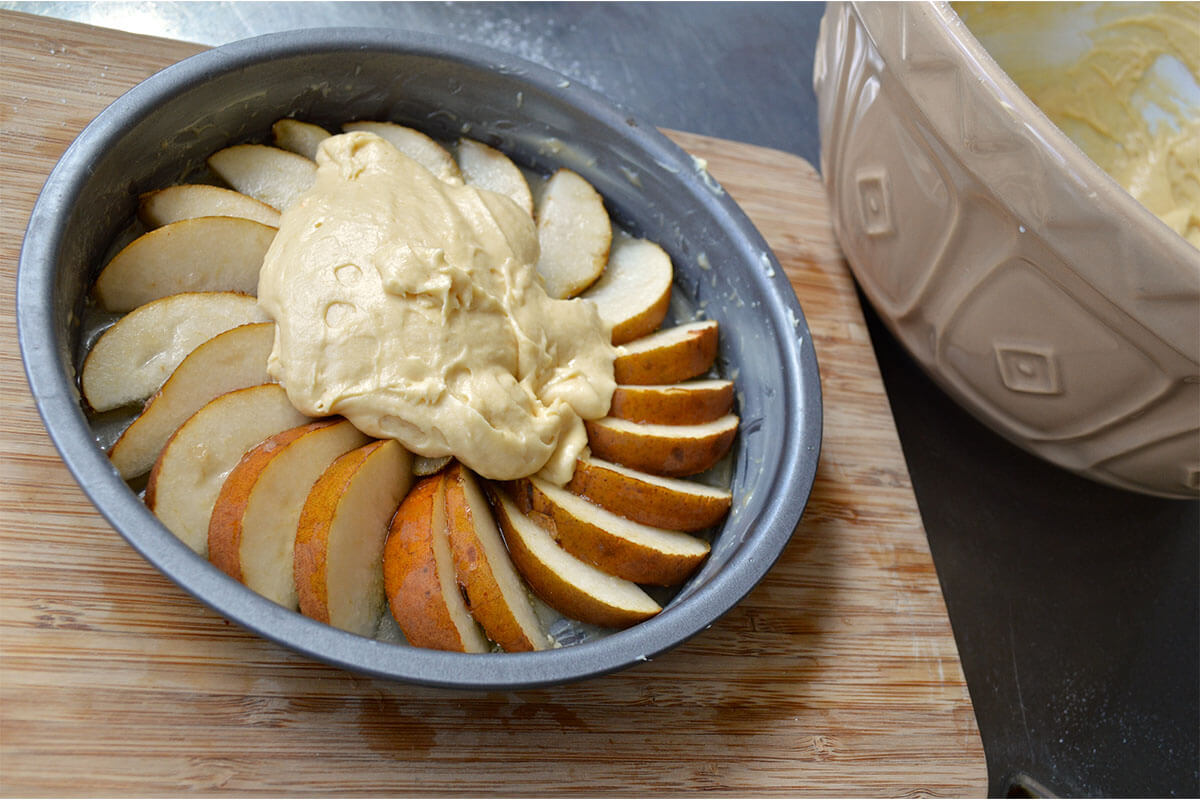 A greased cake tin with some sliced pears arranged in a circular arrangement with cake batter on top