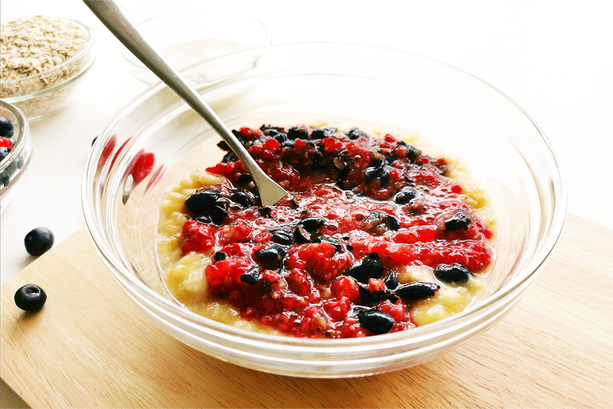 A glass bowl of bananas and berries being mashed together