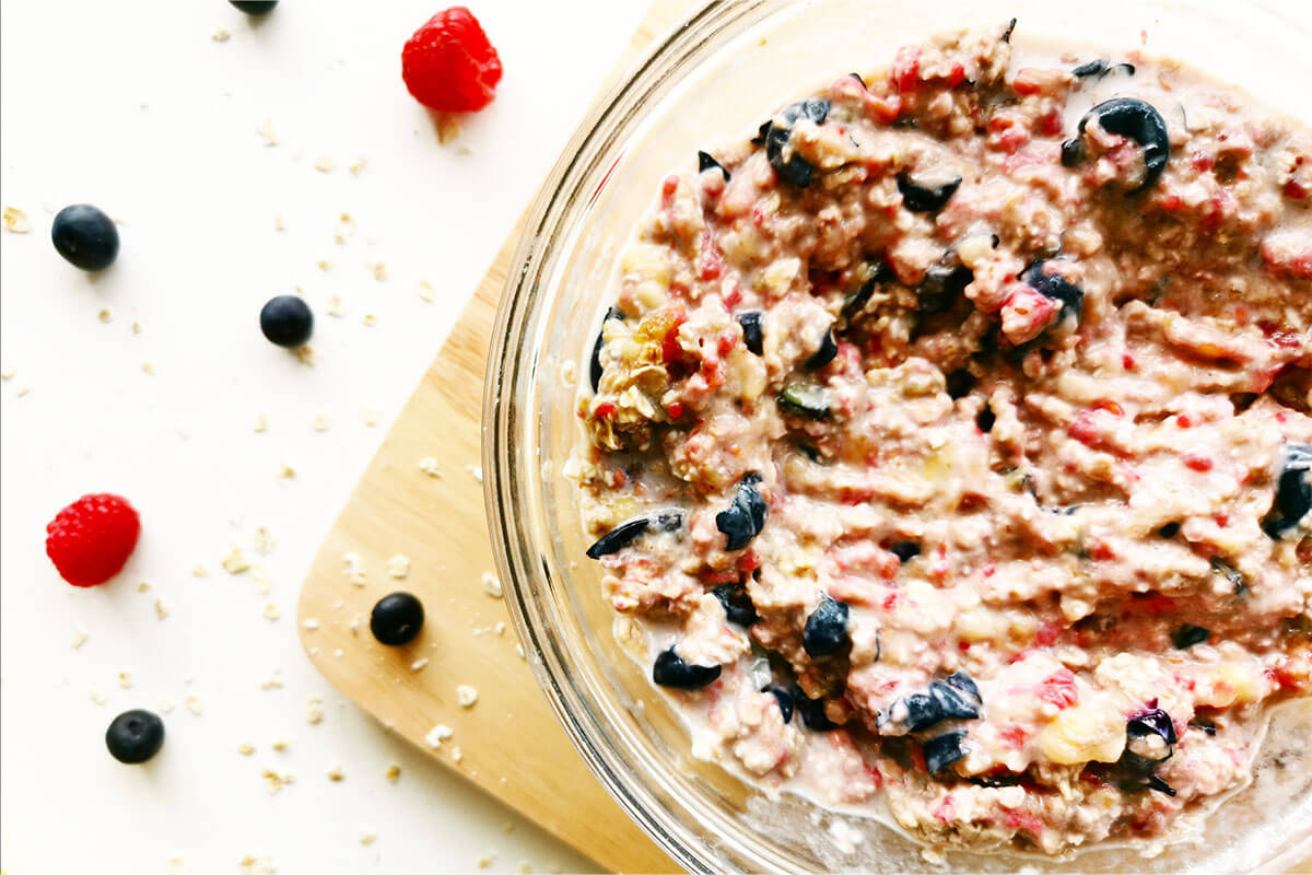 A glass bowl of mashed bananas and berries with added oats