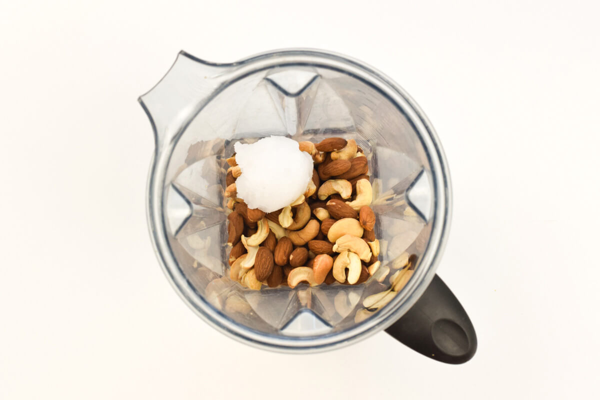 A food processor with roasted almonds and cashews and coconut oil