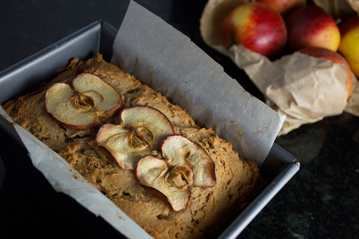 Apple and ginger loaf in a baking tin next to some apples