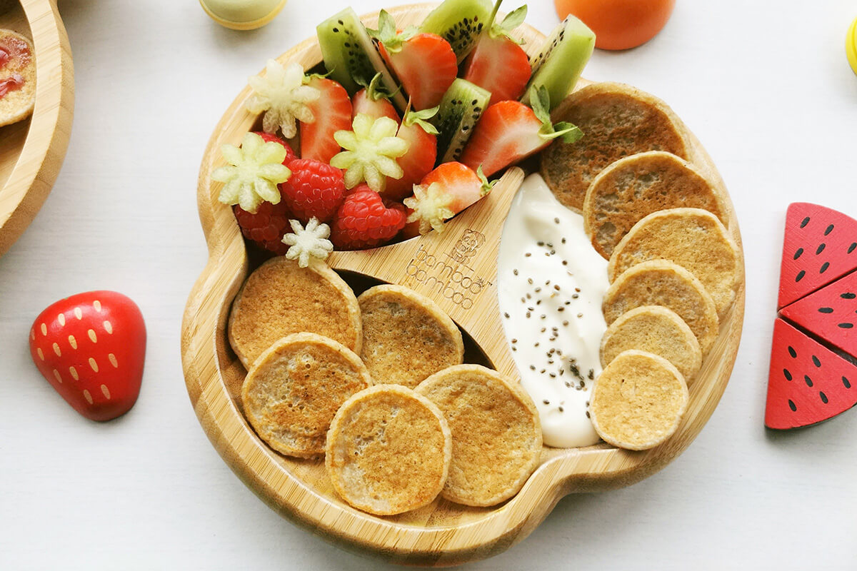 A serving if mini pancakes served with kiwi fruit, strawberries and yoghurt