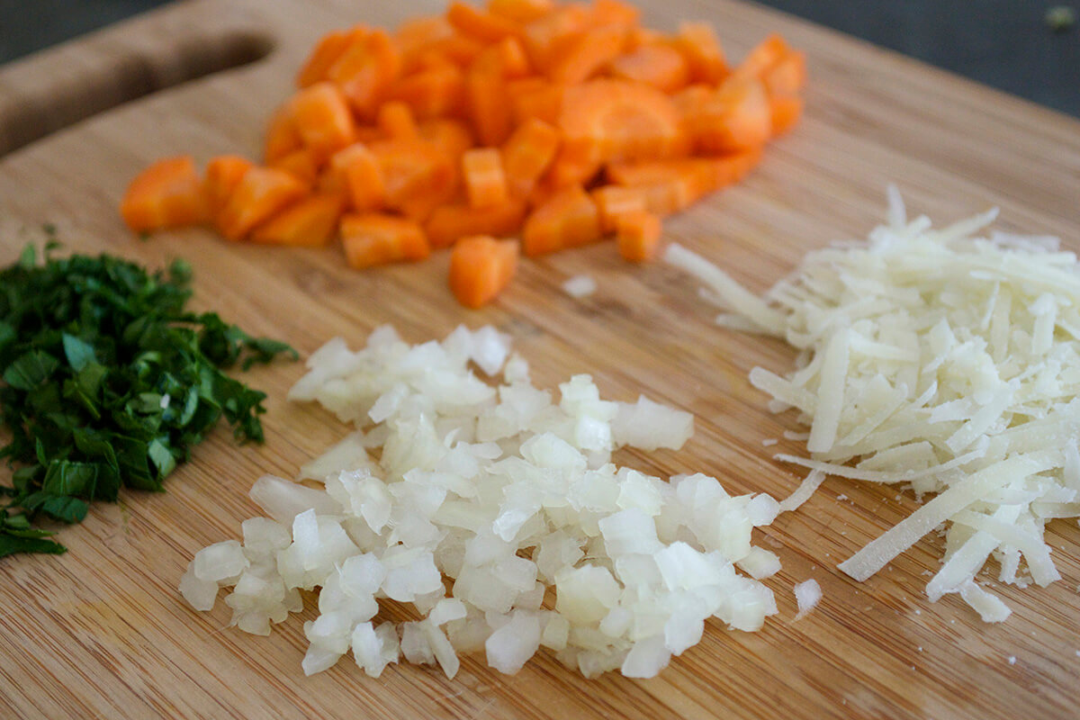 A chopping board with diced sweet potato, onion and herbs