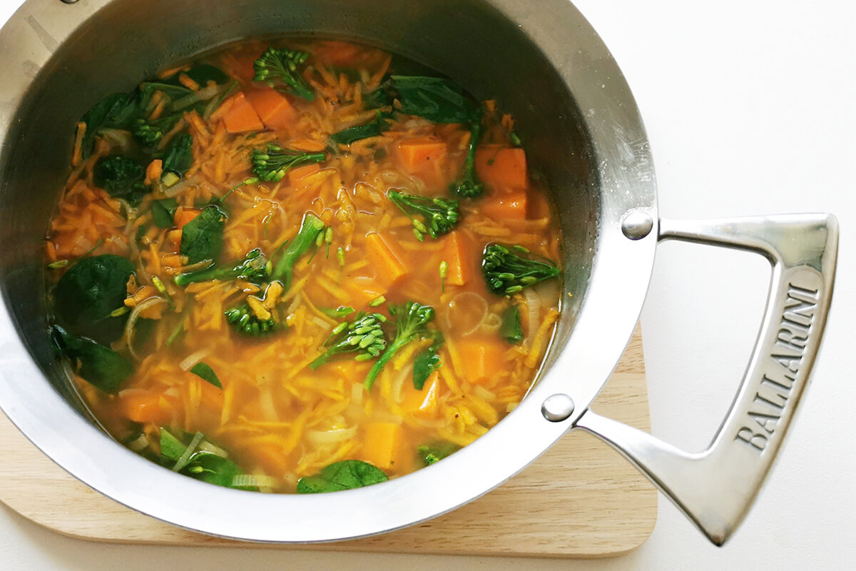 Cubed sweet potato in a saucepan with vegetable stock, grated carrots, broccoli florets and fresh spinach leaves