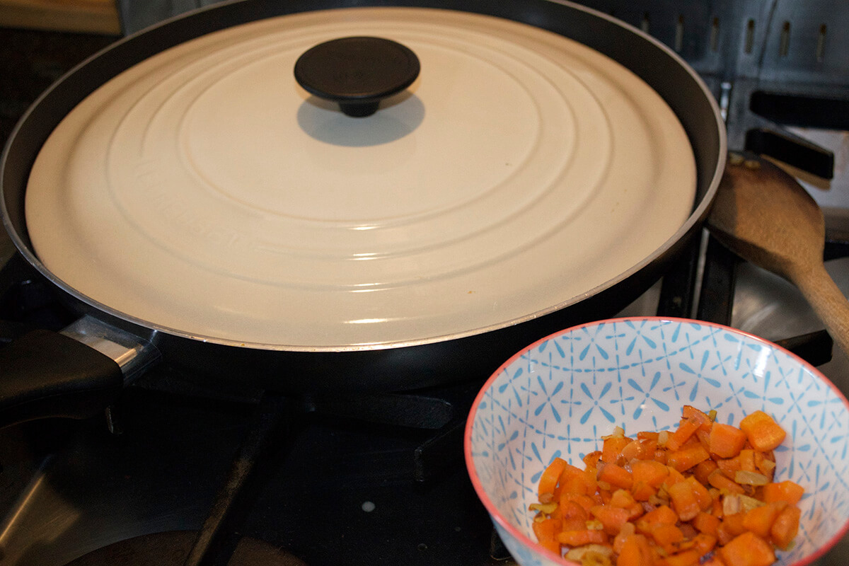 Softened carrot and onion in a bowl next to a covered saucepan