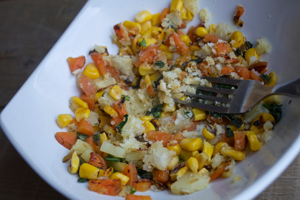 A large bowl of carrot, sweet potato, sweetcorn and herbs being mashed with a fork