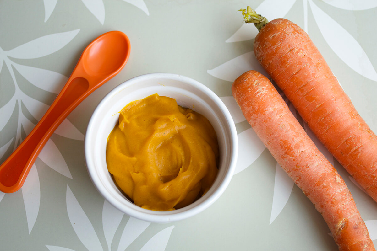 A small bowl of carrot puree next to two carrots